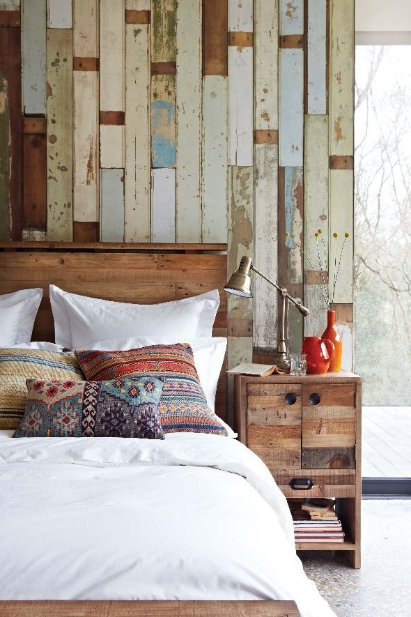 dormitorio con pared de madera despintada, cama y mesa de noche de madera rústica, cojines étnicos