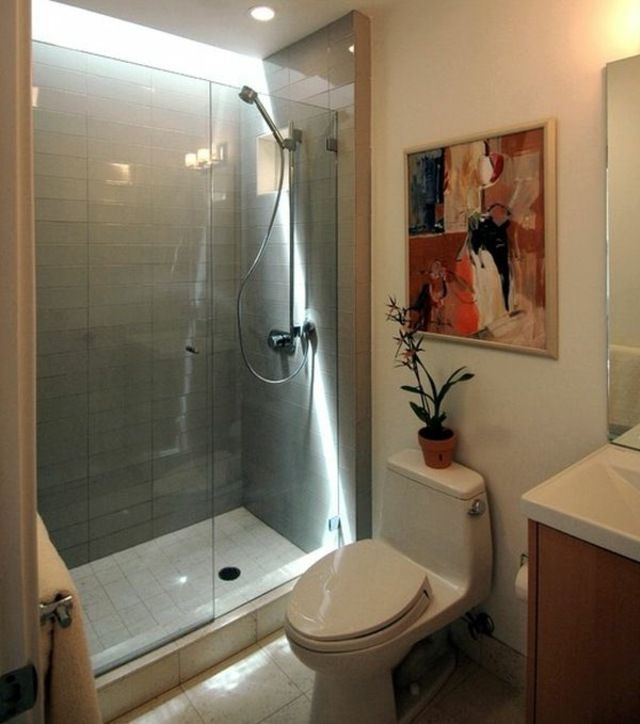Ducha con azulejos grises con mampara transparente, el resto de las paredes del baño son blancas con un cuadro muy colorido