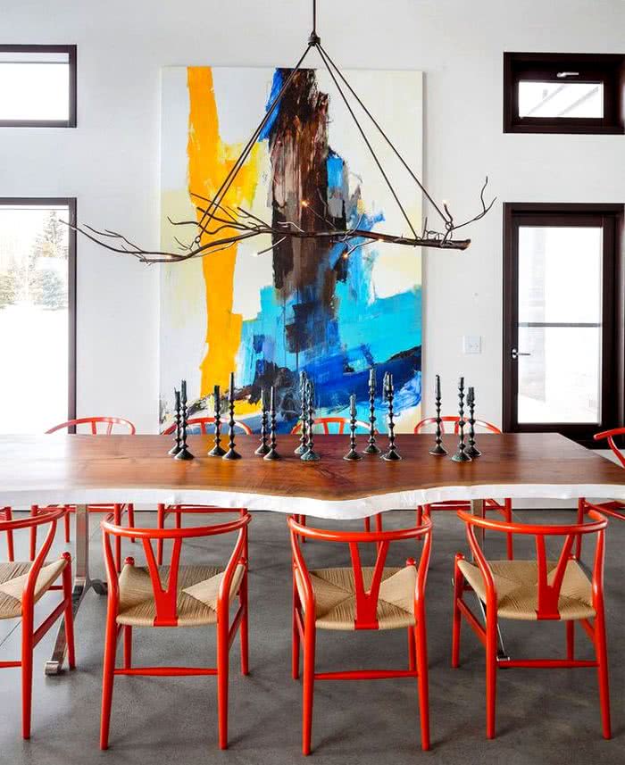 mesa de madera rústica con sillas rojas, pared con cuadro colorido