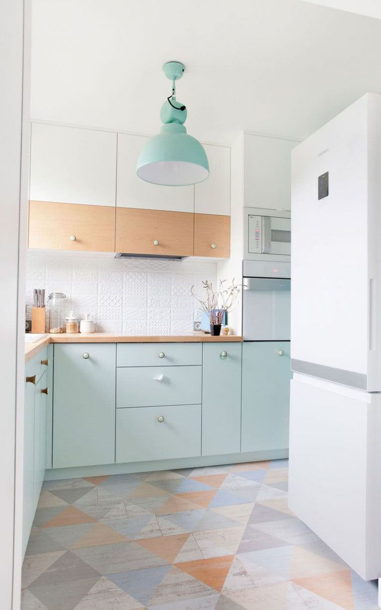 cocina con armarios bajos en color verde menta, paredes blancas, lámpara verde, suelos con diseños geométricos en tonos gris y beige