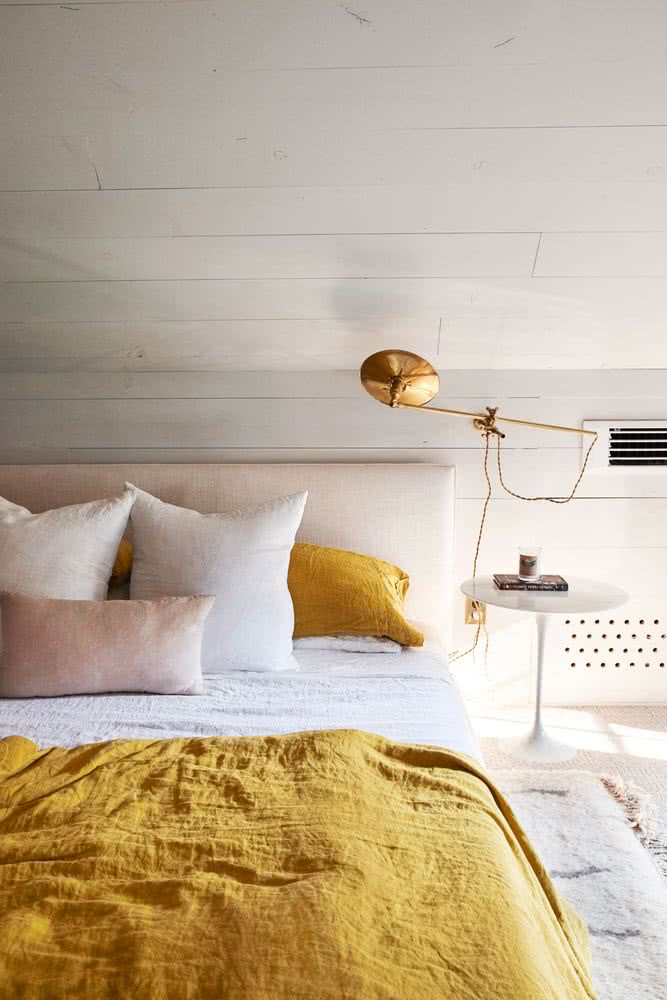 habitación con paredes blancas, lámpara dorada, colcha y cojines amarillo