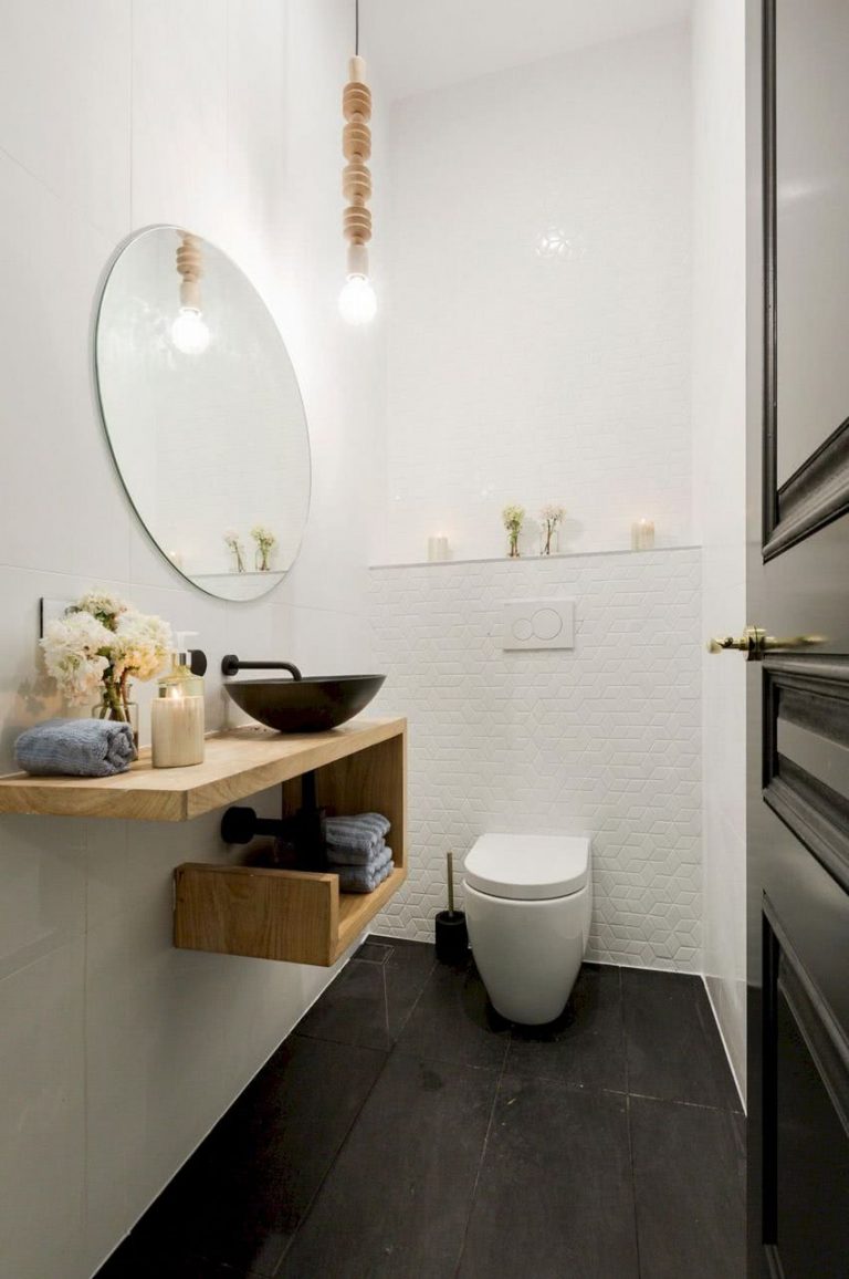 Lavabo sobre encimera de madera con estante flotante, espejo redondeado y un estante de pared con pequeños adornos, paredes blancas y piso negro