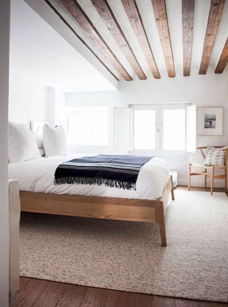 habitación minimalista blanca con cama en madera, y vigas en el techo de madera, alfombra beige