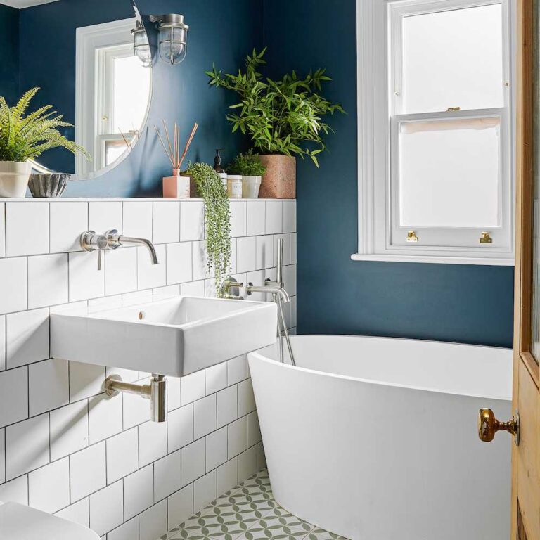 Baño con estante adornado por plantas, azulejos blancos y pared azul