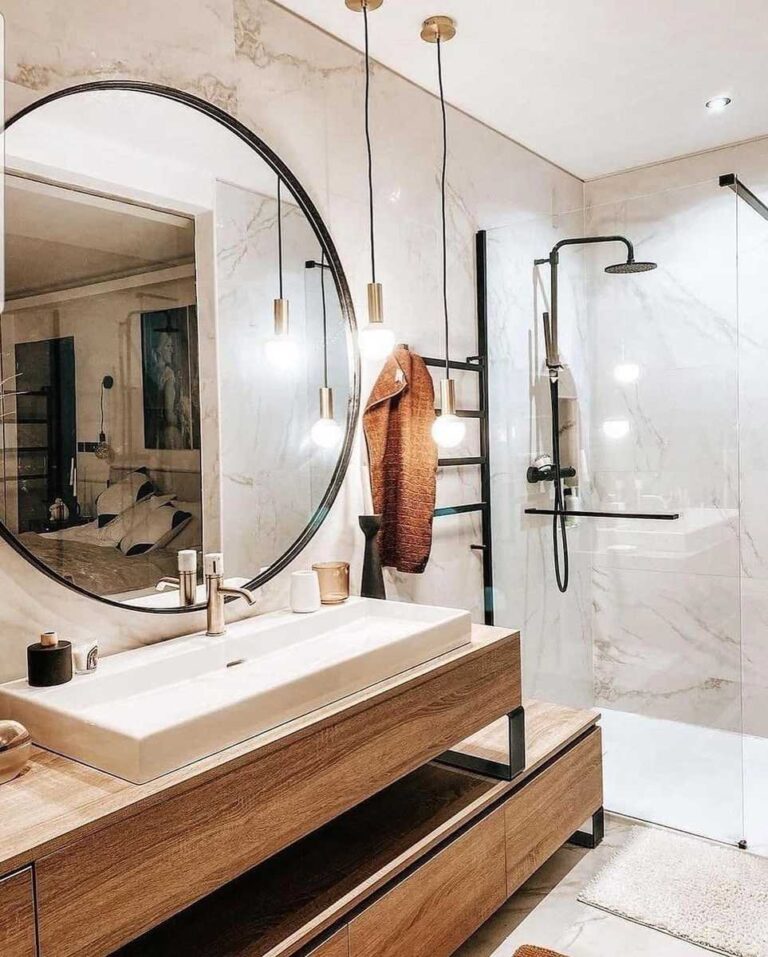 baño con ducha con mampara transparente, espejo redondo y mueble bajo de madera