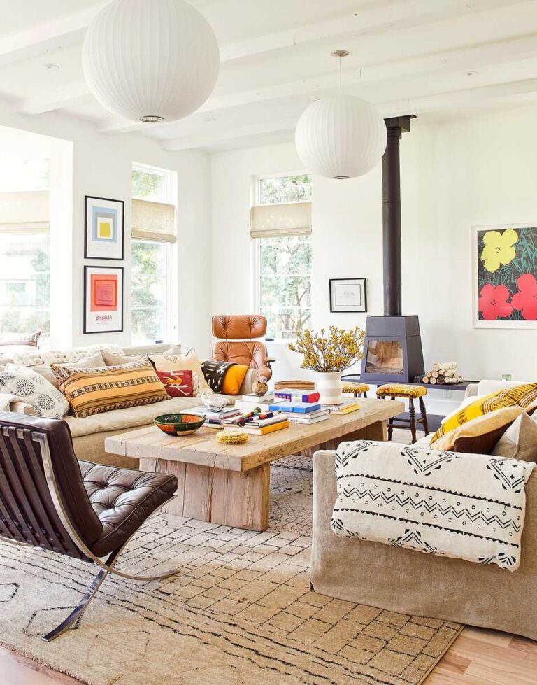 salón con paredes y techo blanco, mesa de centro de madera, sillones y sofá beige, cojines amarillos y rojos