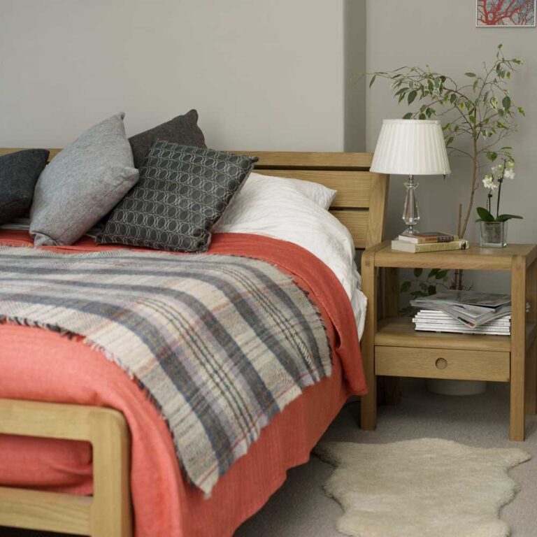 cama de madera, cubrecama naranja, cojines y paredes en gris