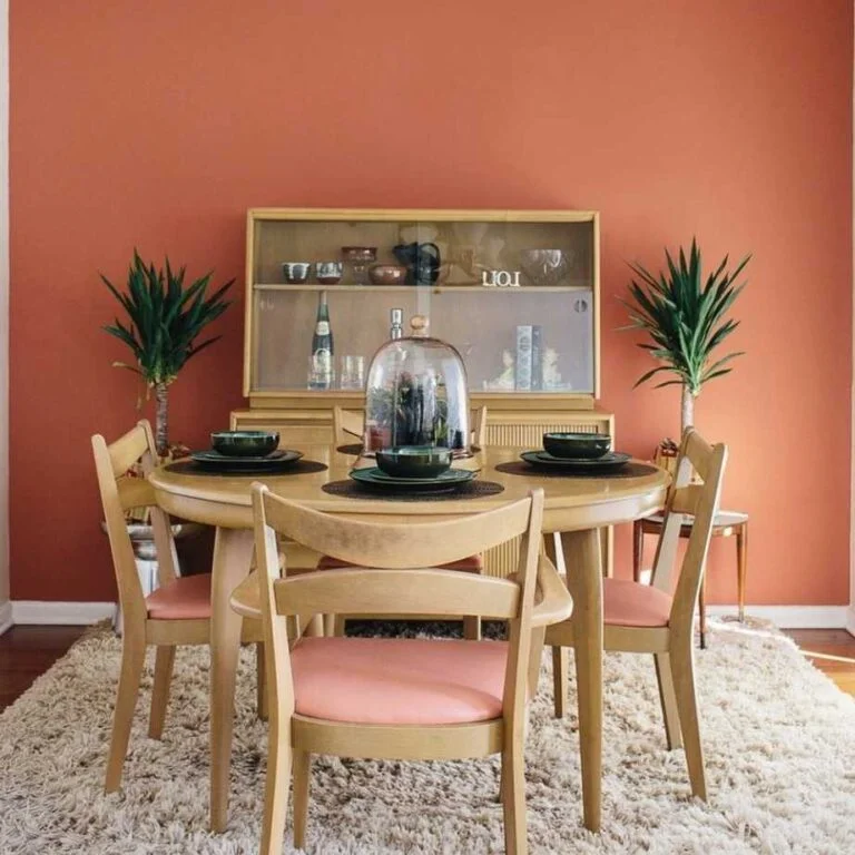 Comedor con pared terracota, mesa y sillas en madera, tapizadas en color rosa, alfombra beige.