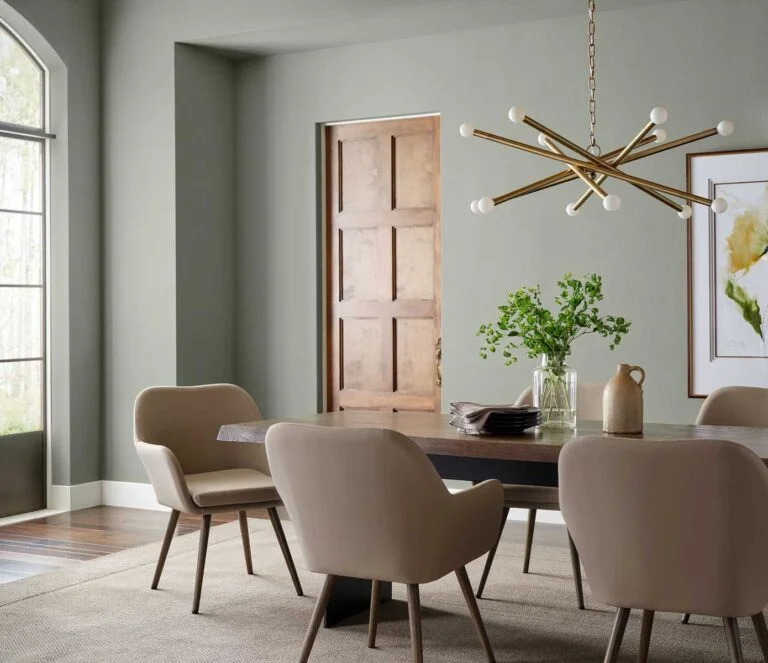 mesa de comedor de madera, sillas tapizadas. Puerta en madera, lámpara colgante de metal, paredes grisáceas