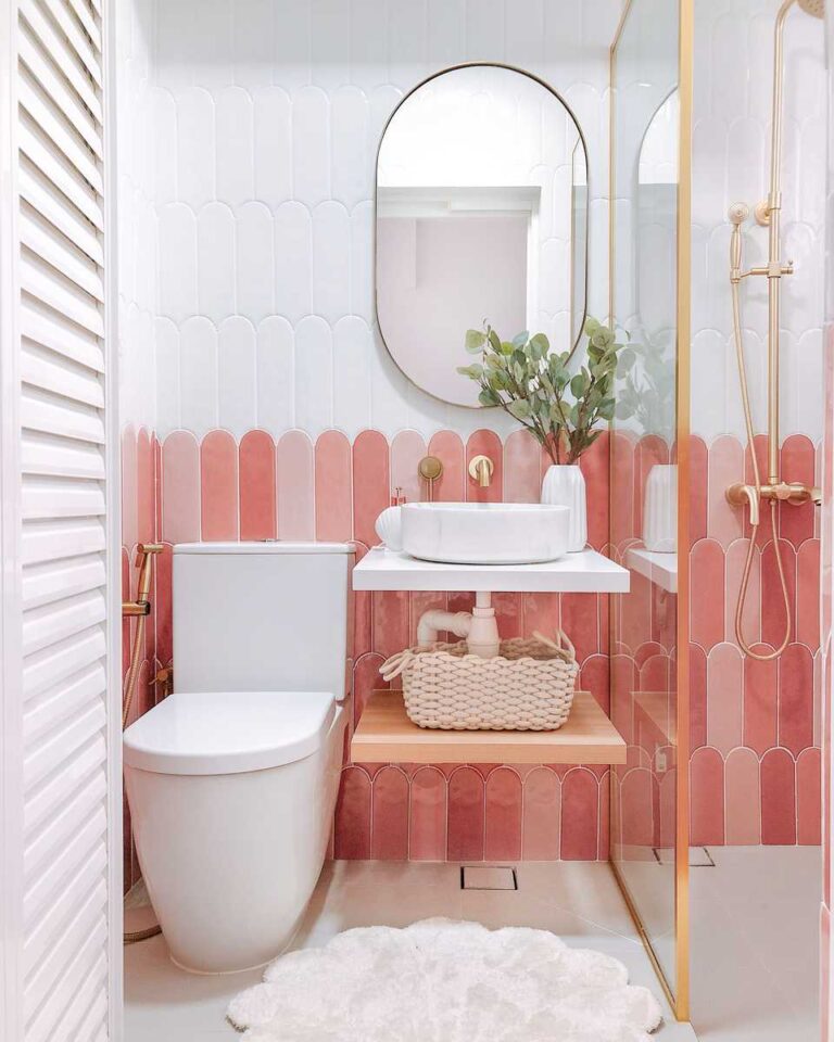 Azulejos en forma de escamas en color blanco y tonos de rosado, lavabo pequeño sobre soporte flotante, inodoro blanco y ducha con mampara